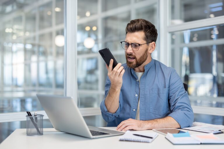 Mann guckt genervt auf sein Handy, weil versteckte Kosten auf ihn zukommen