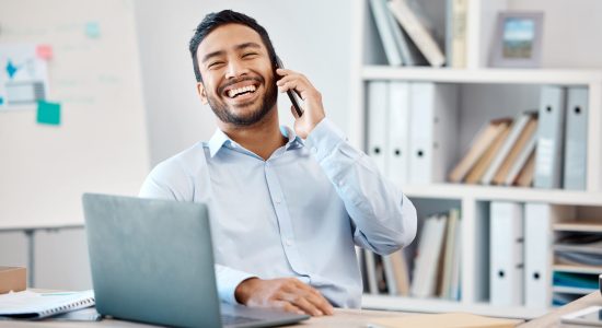 Happy businessman on a phone call while working on a laptop at the desk in his modern office. Corporate, professional and company manager laughing while having a mobile conversation with technology